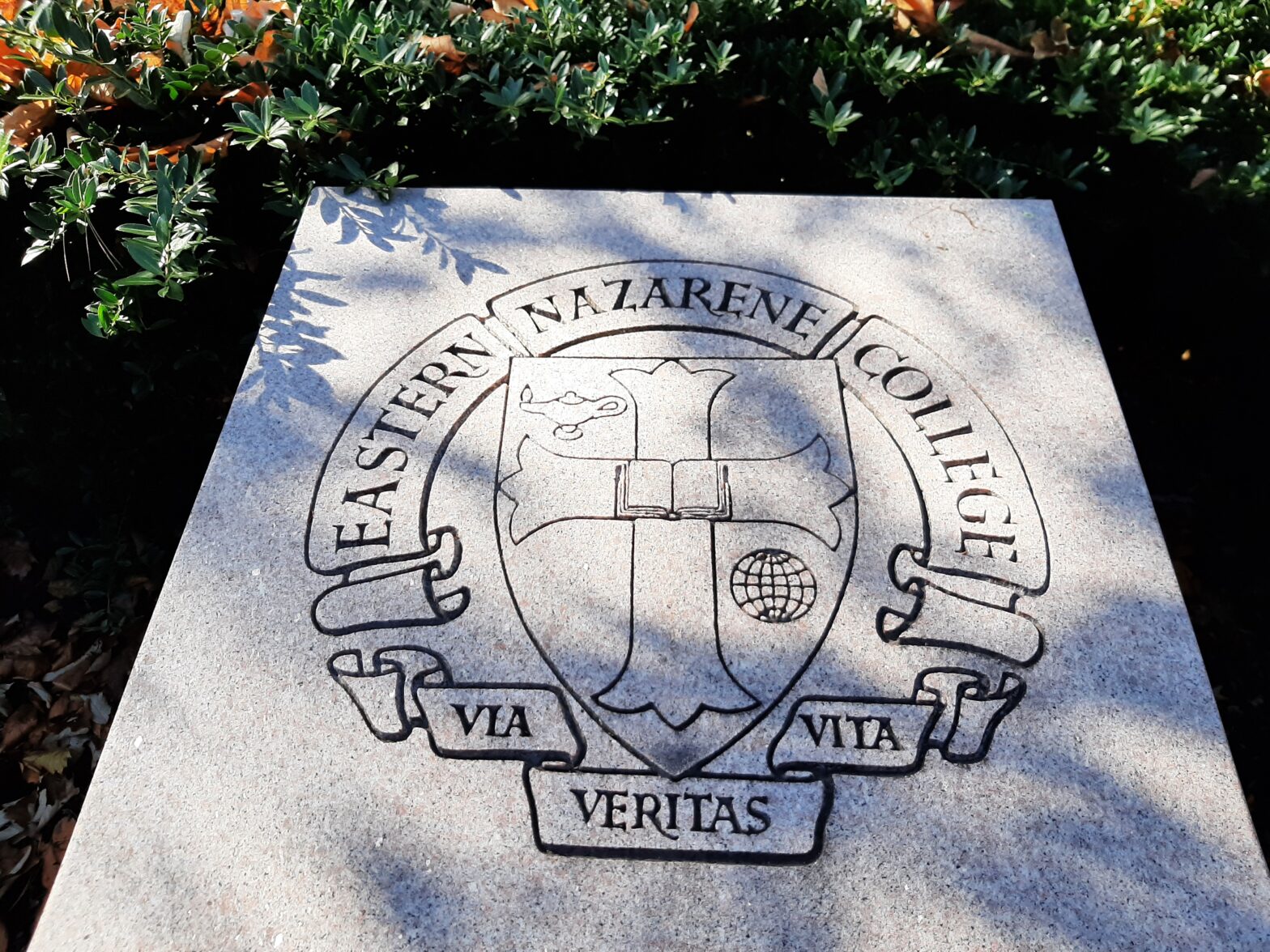 Stone plaque with emblem and motto under sunlight.