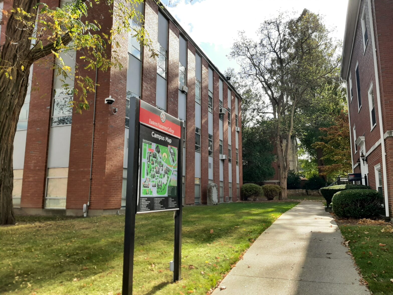 Campus pathway with informational sign next to a brick building.